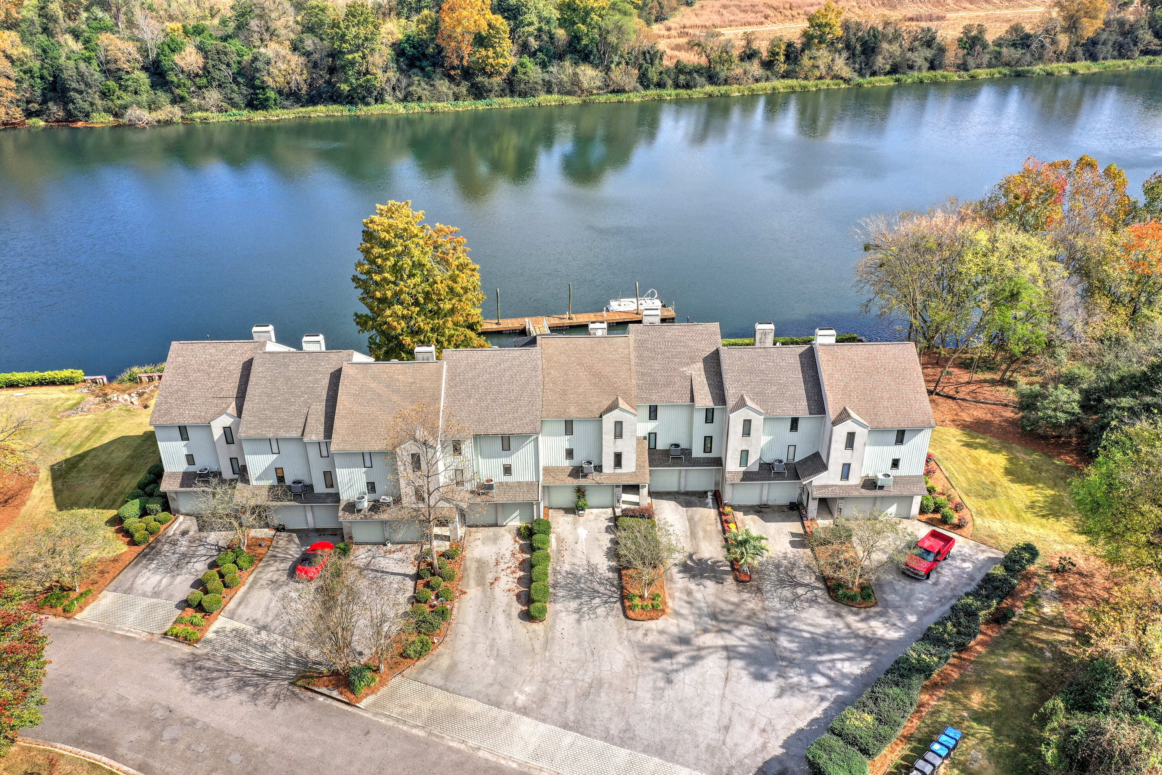 A multi-story residential building with a dock extending into a lake, surrounded by well-maintained lawns and trees.