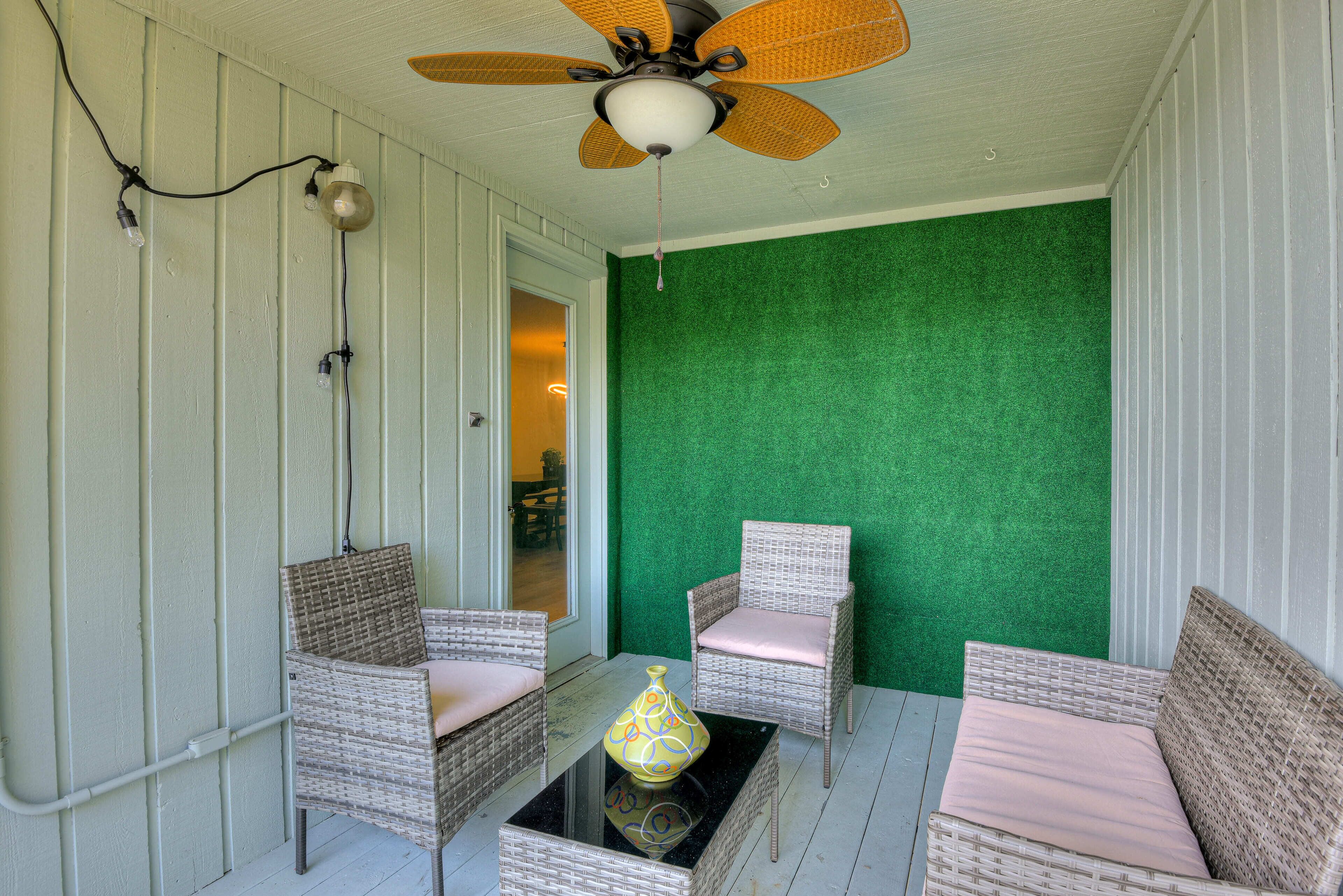 Een overdekt terras met rieten meubels, een plafondventilator en een groene wand.