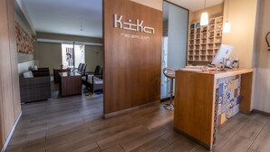 A reception area with a wooden reception desk, a computer, and a shelving unit with various items. - Hotel Kika (Santa Marta)
