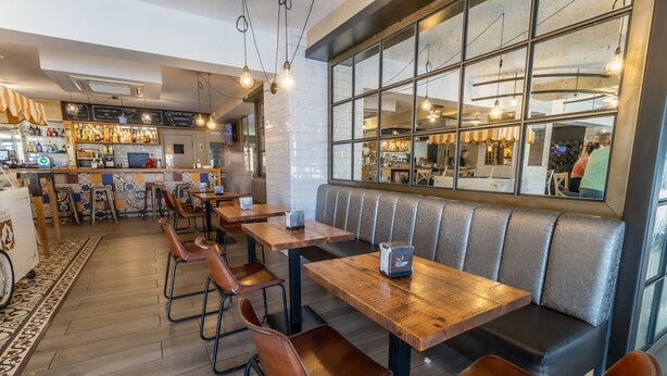 A restaurant interior with wooden tables and leather booths, a bar area with bottles, and a large window with a view of the street. - Hotel Kika (Santa Marta)