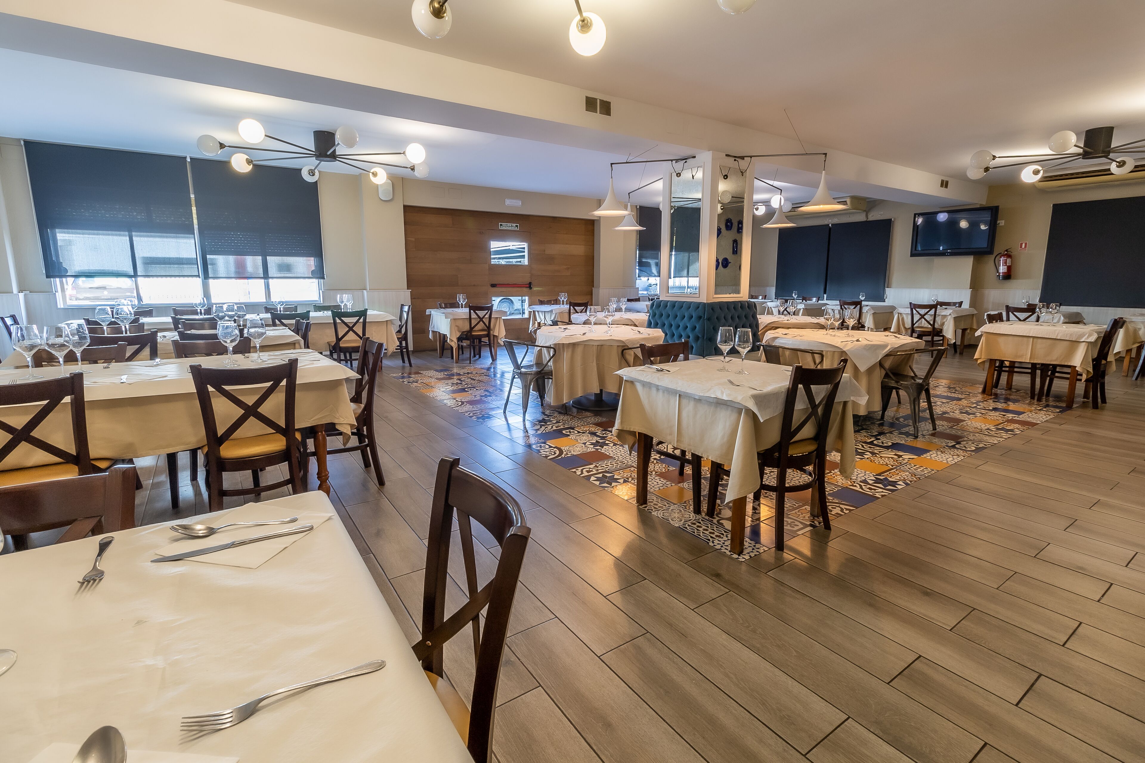 Un restaurante espacioso con varias mesas y sillas, suelo estampado y ventiladores de techo.