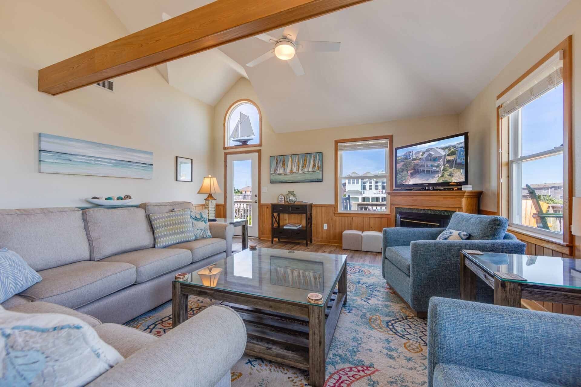 A spacious living room with a high ceiling, a fireplace, and large windows offering a view of the outside.