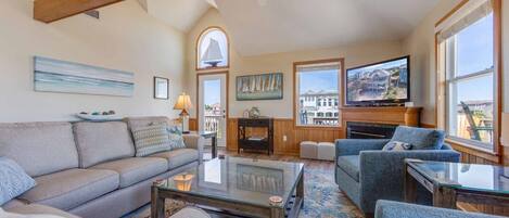 A spacious living room with a high ceiling, a fireplace, and large windows offering a view of the outside.