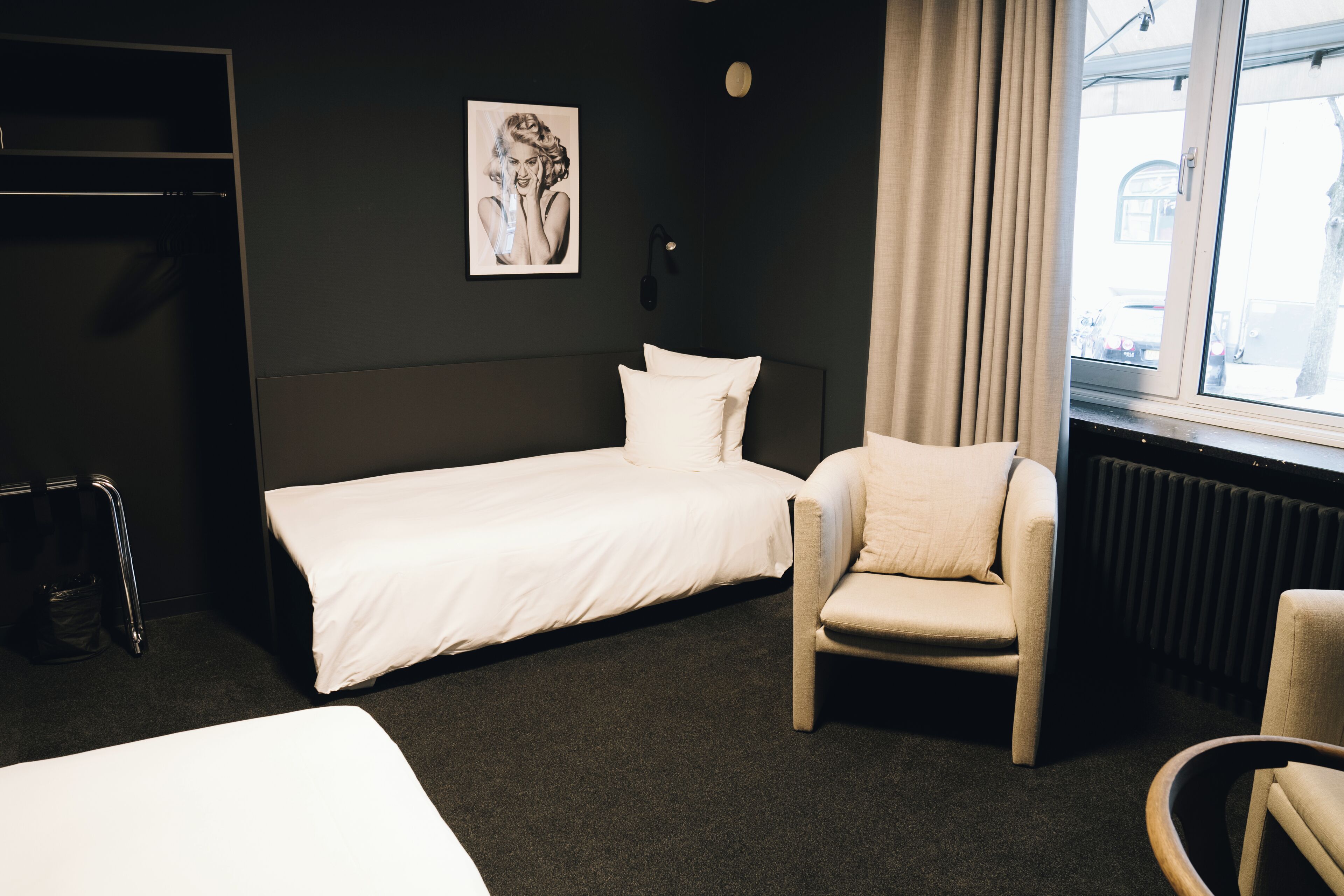 A hotel room with a single bed, a chair, a radiator, and a window with a view.