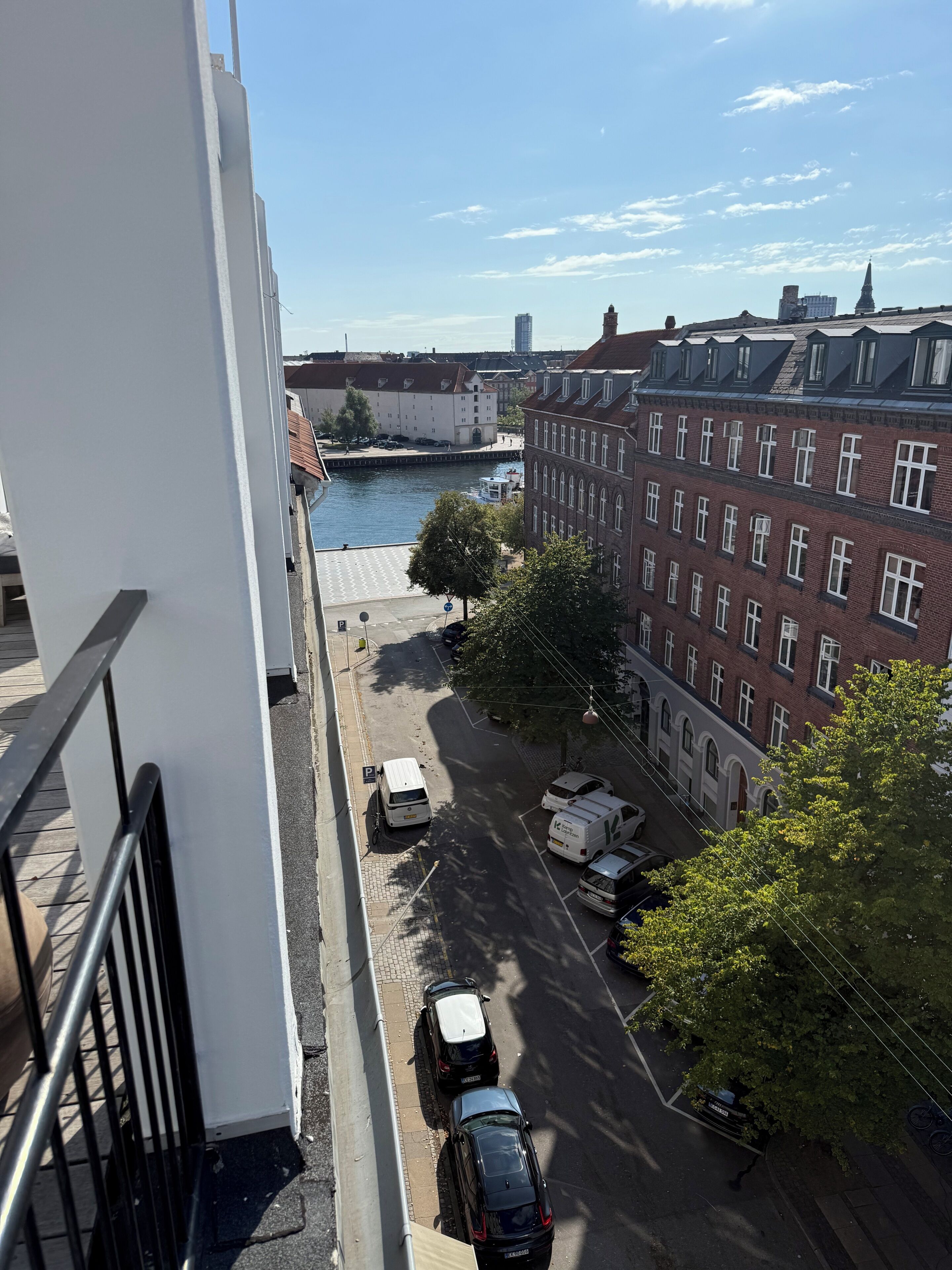 Une vue d’une rue de la ville, avec des immeubles, une rivière et des véhicules garés.