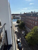 A view of a city street with buildings, a river, and parked vehicles.