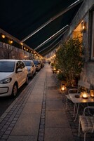 A paved pathway lined with parked cars, outdoor seating, and potted plants.