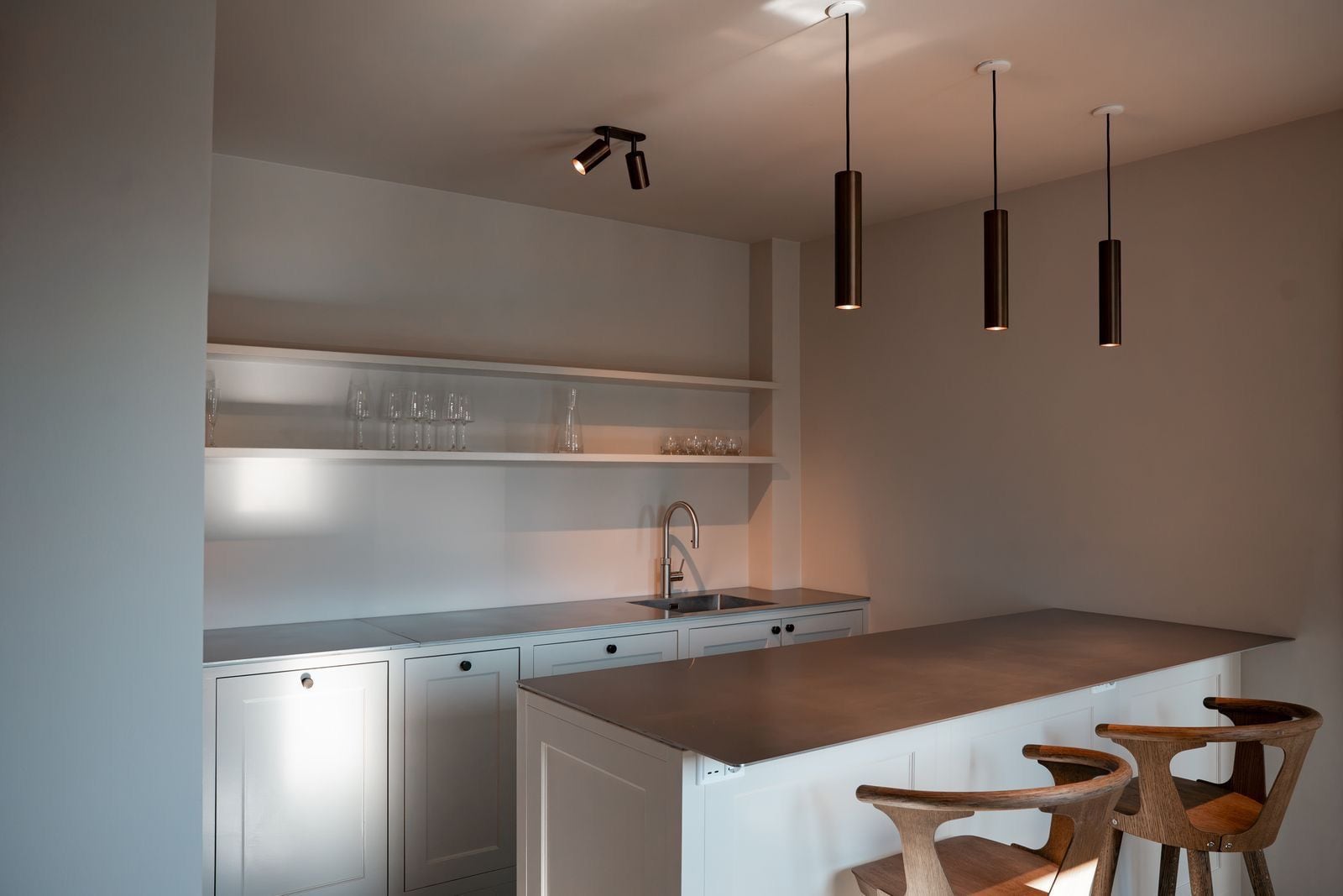 A modern kitchen with a central island, pendant lights, and wooden chairs.