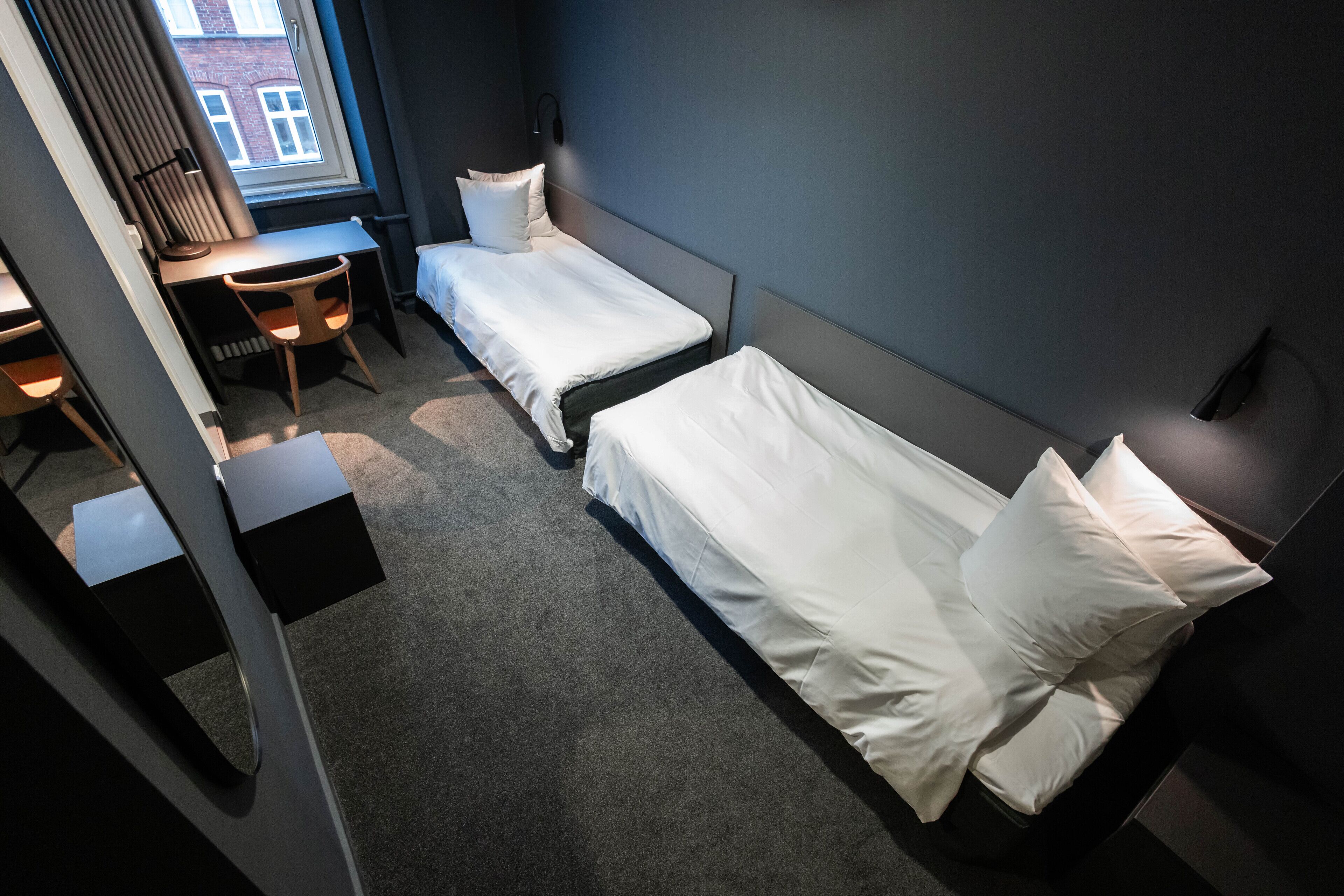 Habitación de hotel con dos camas individuales, un escritorio y una silla.