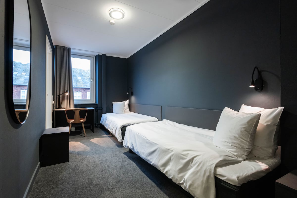 A hotel room with two beds, a desk, a chair, and a large window.