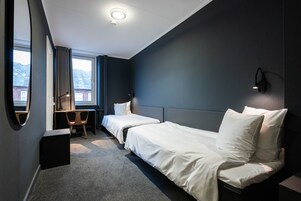 A hotel room with two beds, a desk, a chair, and a large window.