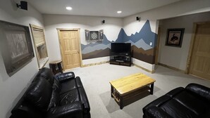 A living room with a TV, two black leather sofas, a wooden coffee table, and a mountain mural on the wall. - Experience the Magic of Wapiti Valley in Luxury. Stunning Views-East Yellowstone (Cody)