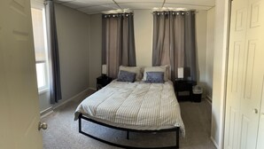 A bedroom with a bed, two bedside tables, a window with curtains, and a door. - Downtown Getaway 2 (Michigan City)