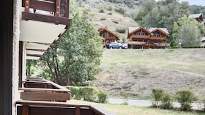 Una terraza de madera con una mesa y sillas, con vistas a una colina con cabañas de madera.