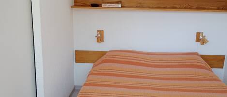 Un dormitorio con cama, cabecera de madera y manta a rayas.