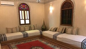 Um quarto com dois sofás, um tapete vermelho estampado e janelas decorativas.