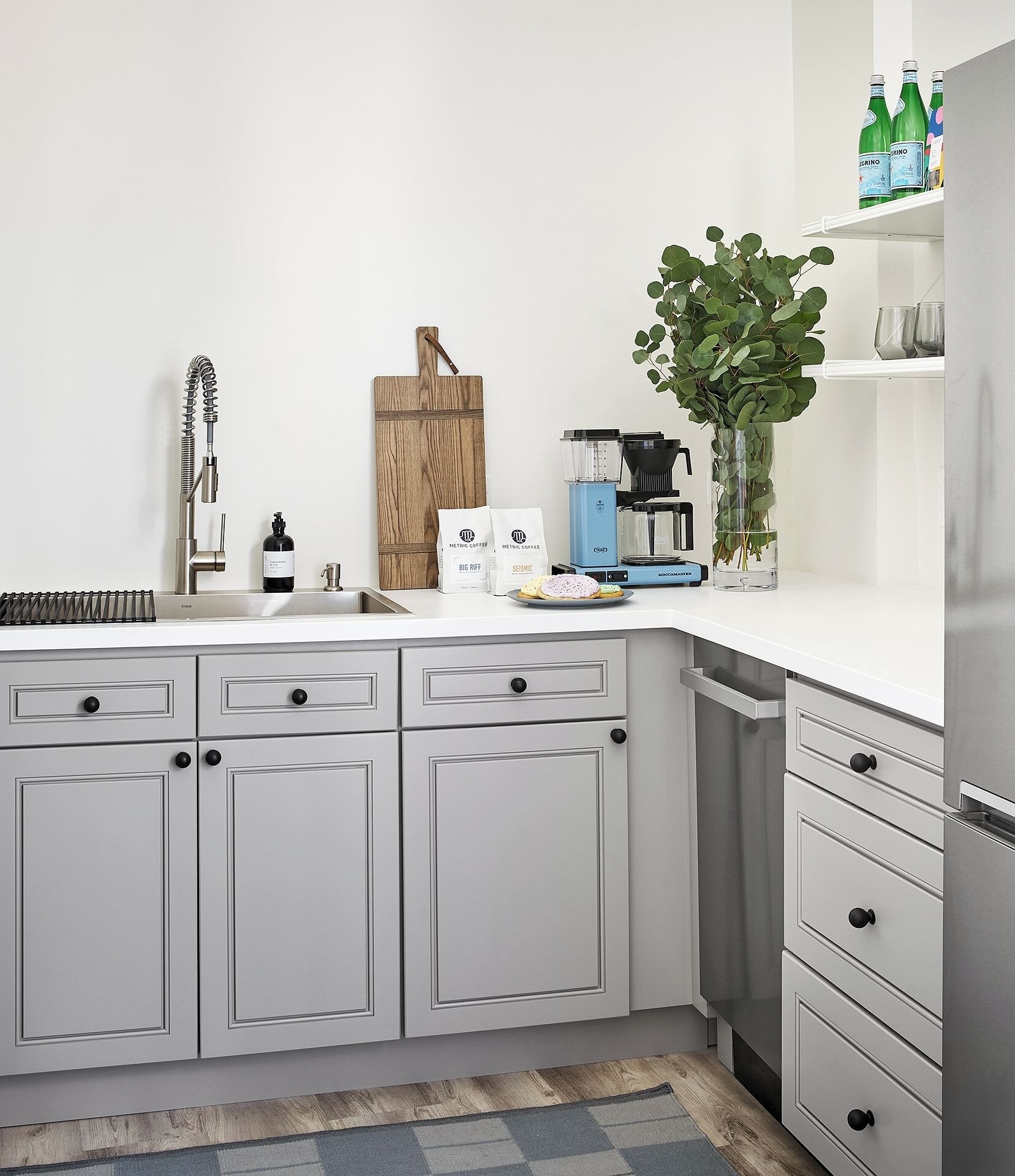 A modern kitchen with grey cabinets, a coffee machine, a cutting board, and a potted plant.