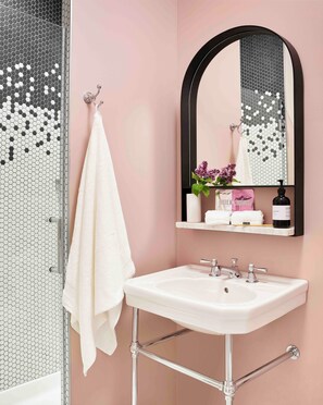Un baño con un lavamanos blanco, un espejo y una ducha con un patrón de azulejos hexagonales.