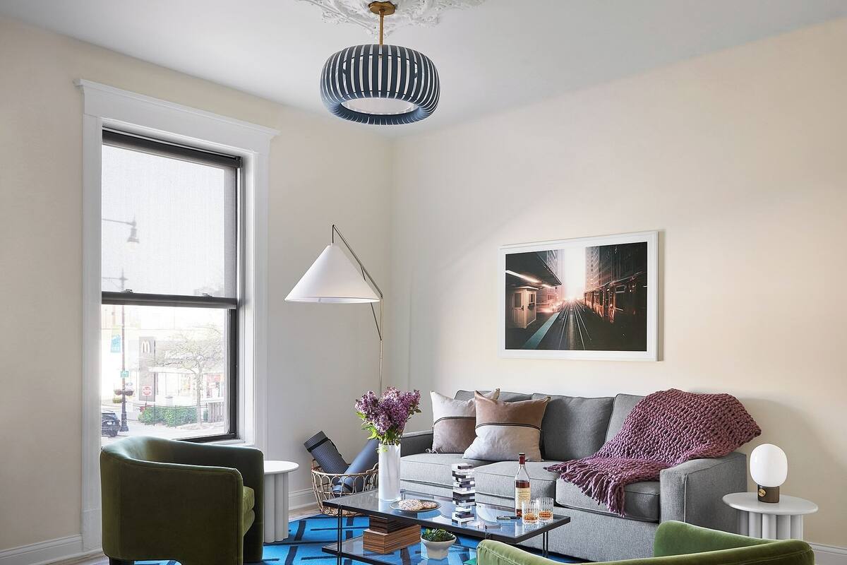 Un salon moderne avec un canapé, des fauteuils verts, une table basse et une grande fenêtre.
