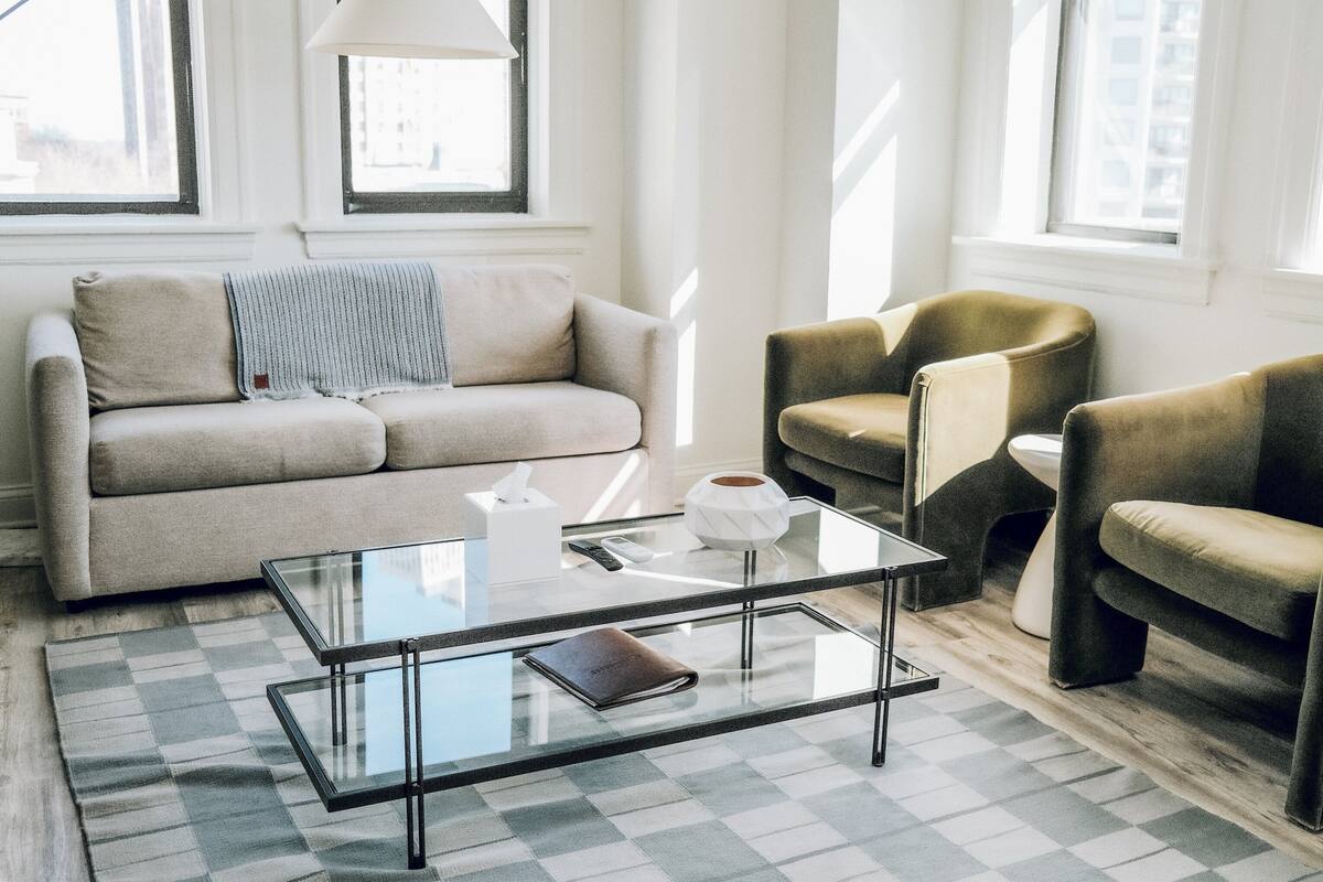 Un salon moderne avec une table basse en verre, un canapé beige et deux fauteuils.