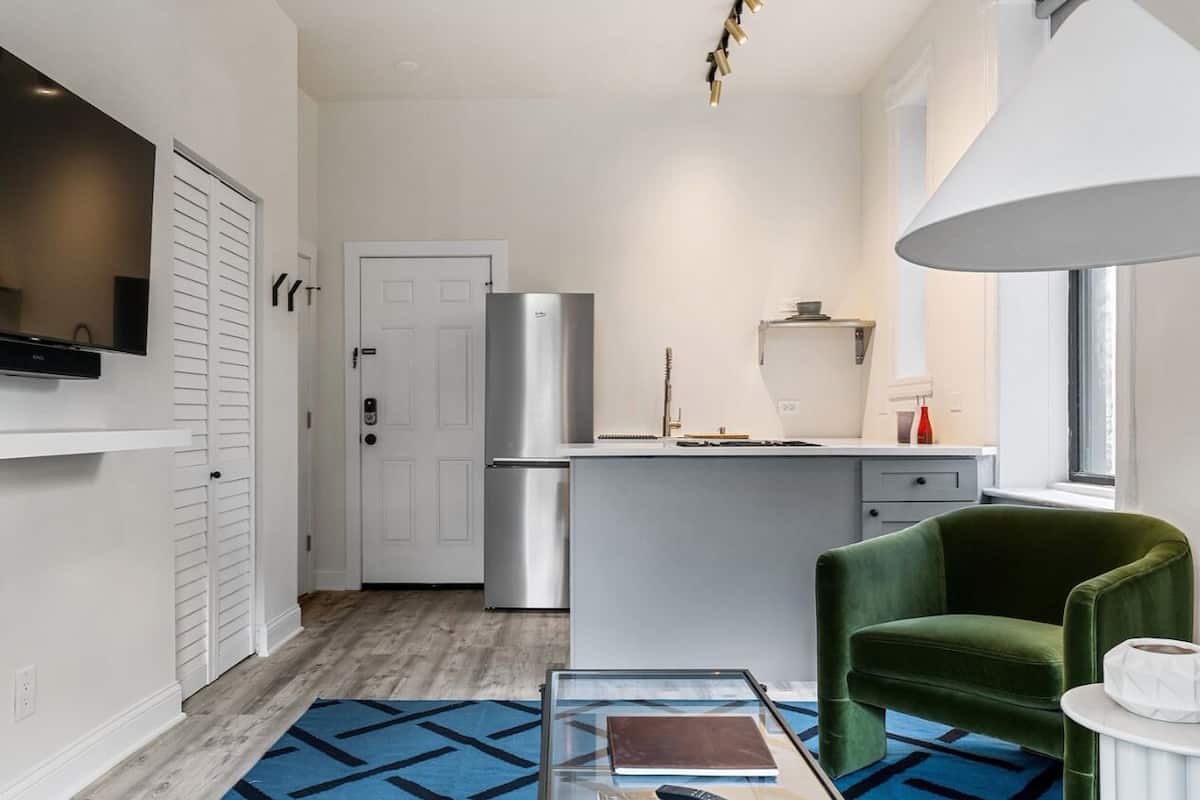 Une cuisine moderne équipée d’un réfrigérateur, d’un coin repas avec une chaise verte et d’une table basse en verre.