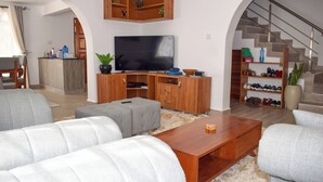Ein Wohnzimmer mit Fernseher, einer Holz-Unterhaltungsecke, grauen Sofas und einer Treppe.