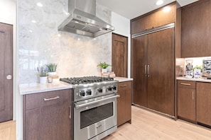 A kitchen with a stainless steel Viking stove, oven, and hood, wooden cabinets, marble backsplash, and a wooden floor. - Walk to Ski Slopes + Trails! Luxury 4-Bedroom Private Home with Private Hot tub, A/C, Heated Parking, and Two Master Suite! | PEA-1009 by KBM Resorts (Park City)