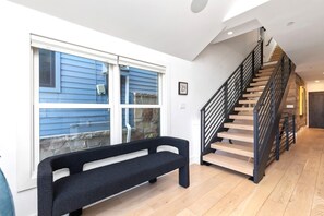 Un intérieur moderne avec un escalier en bois, un banc et une grande fenêtre équipée de stores.