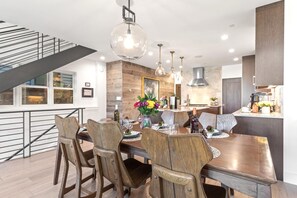 A modern dining area with a wooden table, chairs, and a hanging light fixture. - Walk to Ski Slopes + Trails! Luxury 4-Bedroom Private Home with Private Hot tub, A/C, Heated Parking, and Two Master Suite! | PEA-1009 by KBM Resorts (Park City)