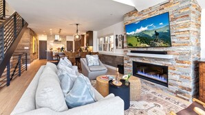Ein Wohnzimmer mit Kamin aus Stein, einem großen, an der Wand befestigten Fernseher und einer Treppe zum Obergeschoss.
