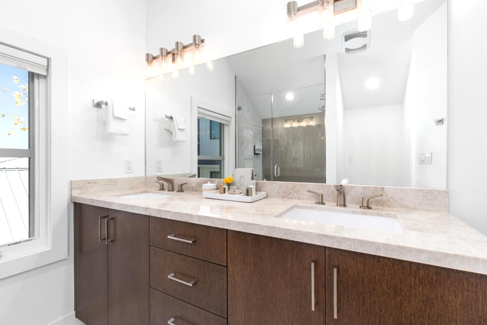 A modern bathroom with two sinks, a large mirror, and a vanity with drawers.