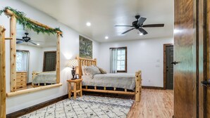 Un dormitorio con cama de madera, ventilador de techo, espejo y suelo de madera.