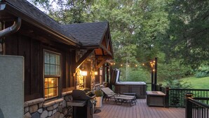 Una terraza de madera con pared de piedra, mobiliario exterior y una parrilla.