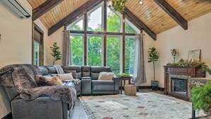 Una sala de estar acogedora con un sofá modular, una chimenea y grandes ventanales que ofrecen vistas al exterior.