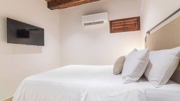 Un dormitorio con cama, televisor montado, equipo de aire acondicionado y ventana con persianas.