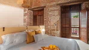Een hotelkamer met een groot bed, houten luiken en een ontbijttafel met croissants, koffie en sinaasappelsap.