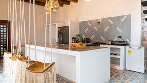 Een moderne keuken met een centraal eiland, hangende macramé-stoelen en een backsplash met een herringbone-patroon.