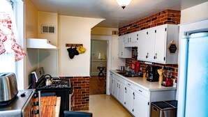 Una cocina pequeña con gabinetes blancos, una pared de ladrillo decorativa y electrodomésticos básicos.