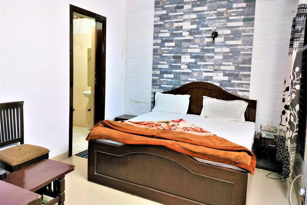 A bedroom with a bed, a wooden nightstand, a chair, a bedside table, and a wall with a patterned design.