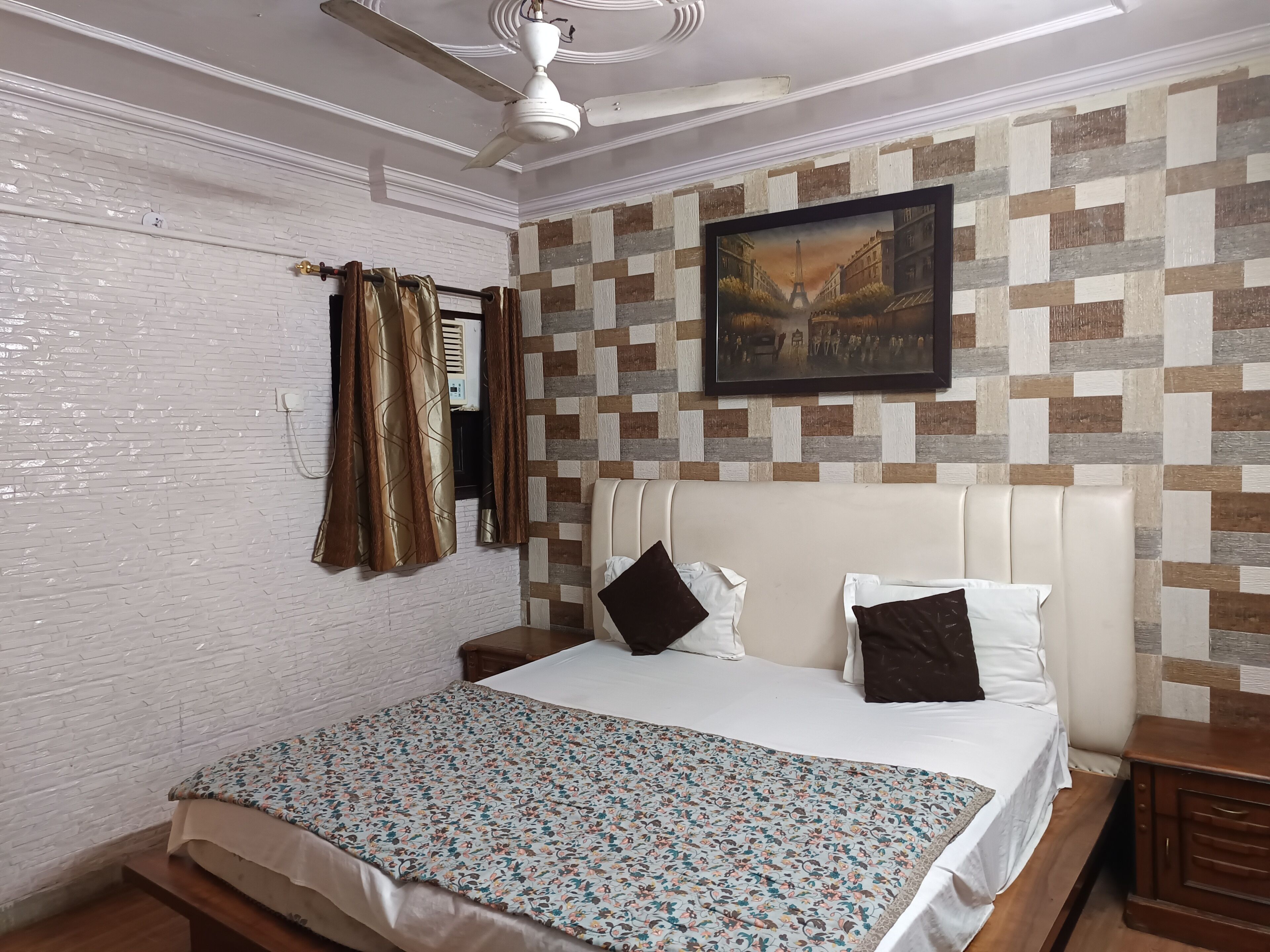 A bedroom with a bed, a ceiling fan, a painting, and a patterned wall.