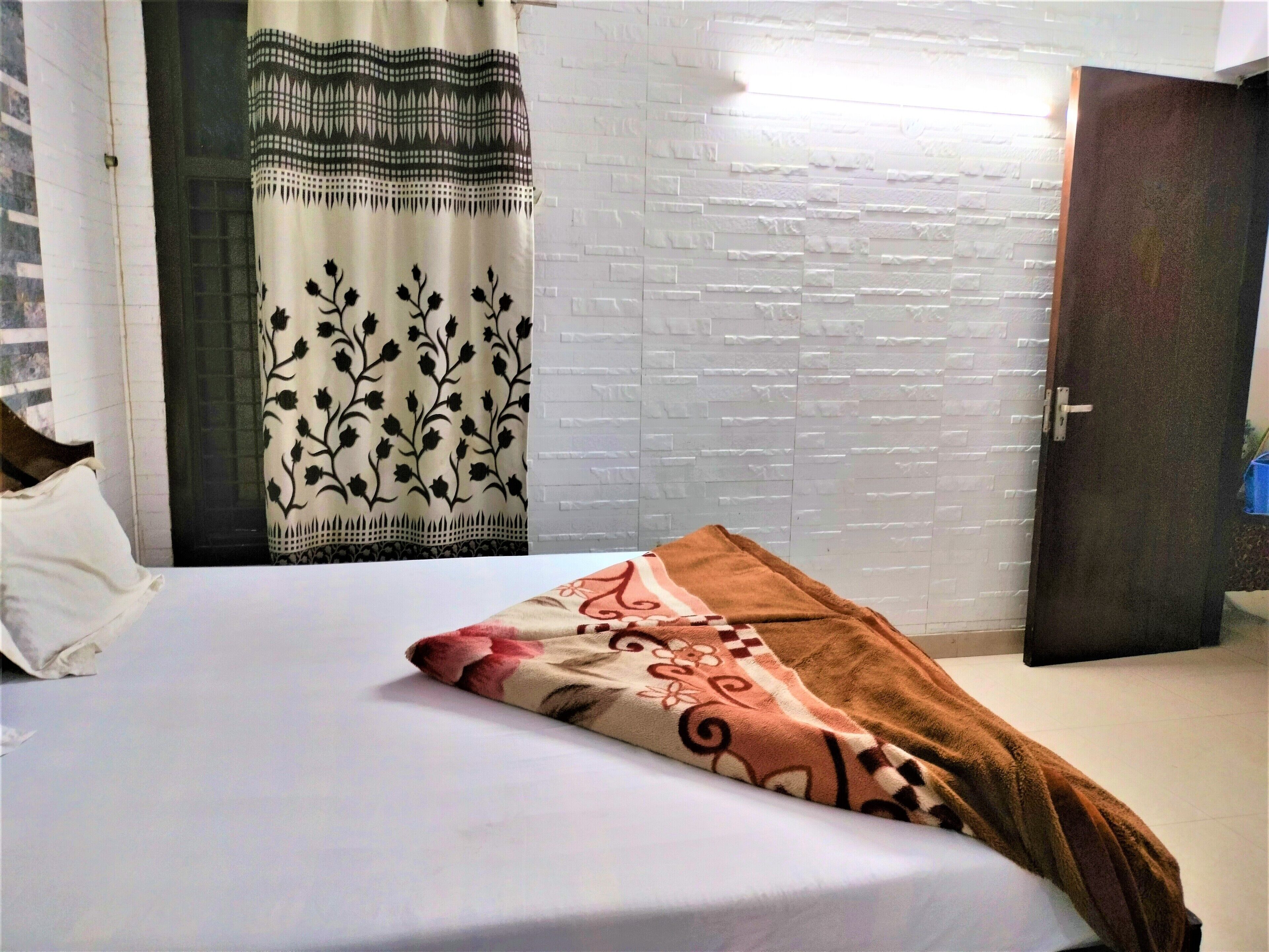 A bedroom with a bed, a white brick wall, a door, and a curtain with a floral pattern.