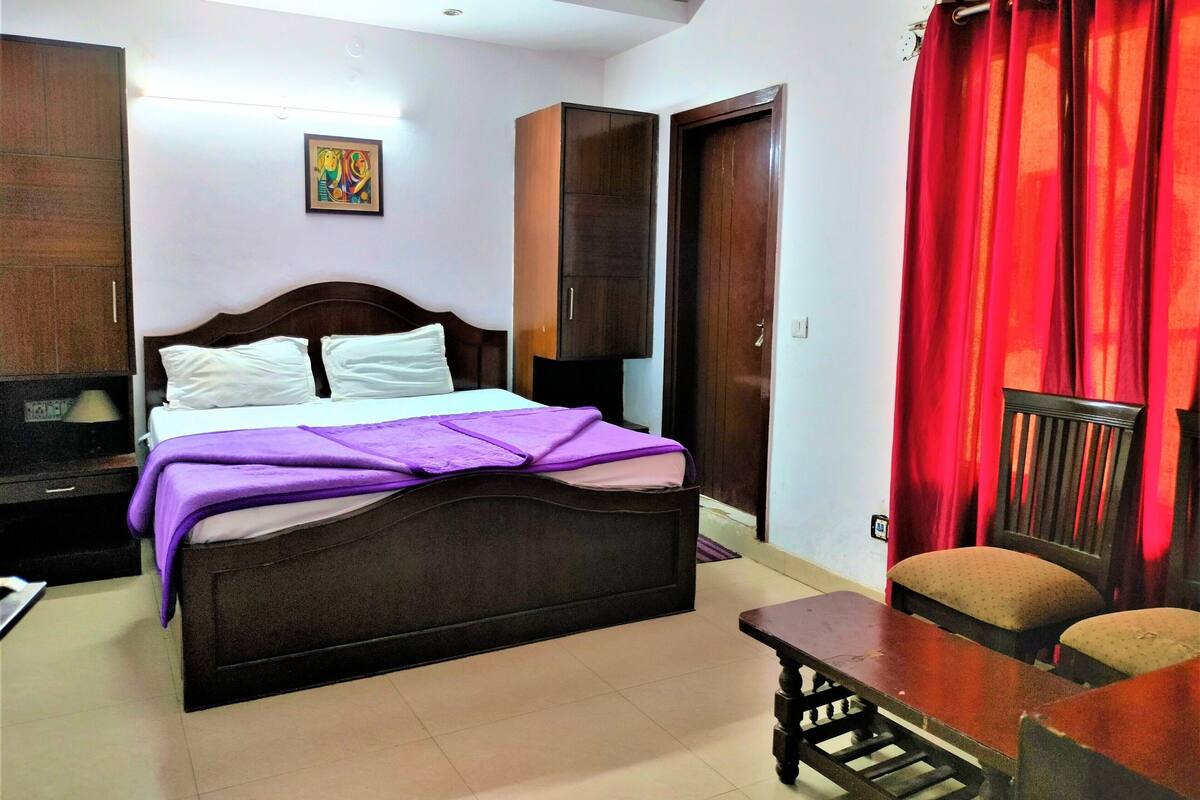 A bedroom with a bed, a desk, a chair, a wardrobe, and a red curtain.