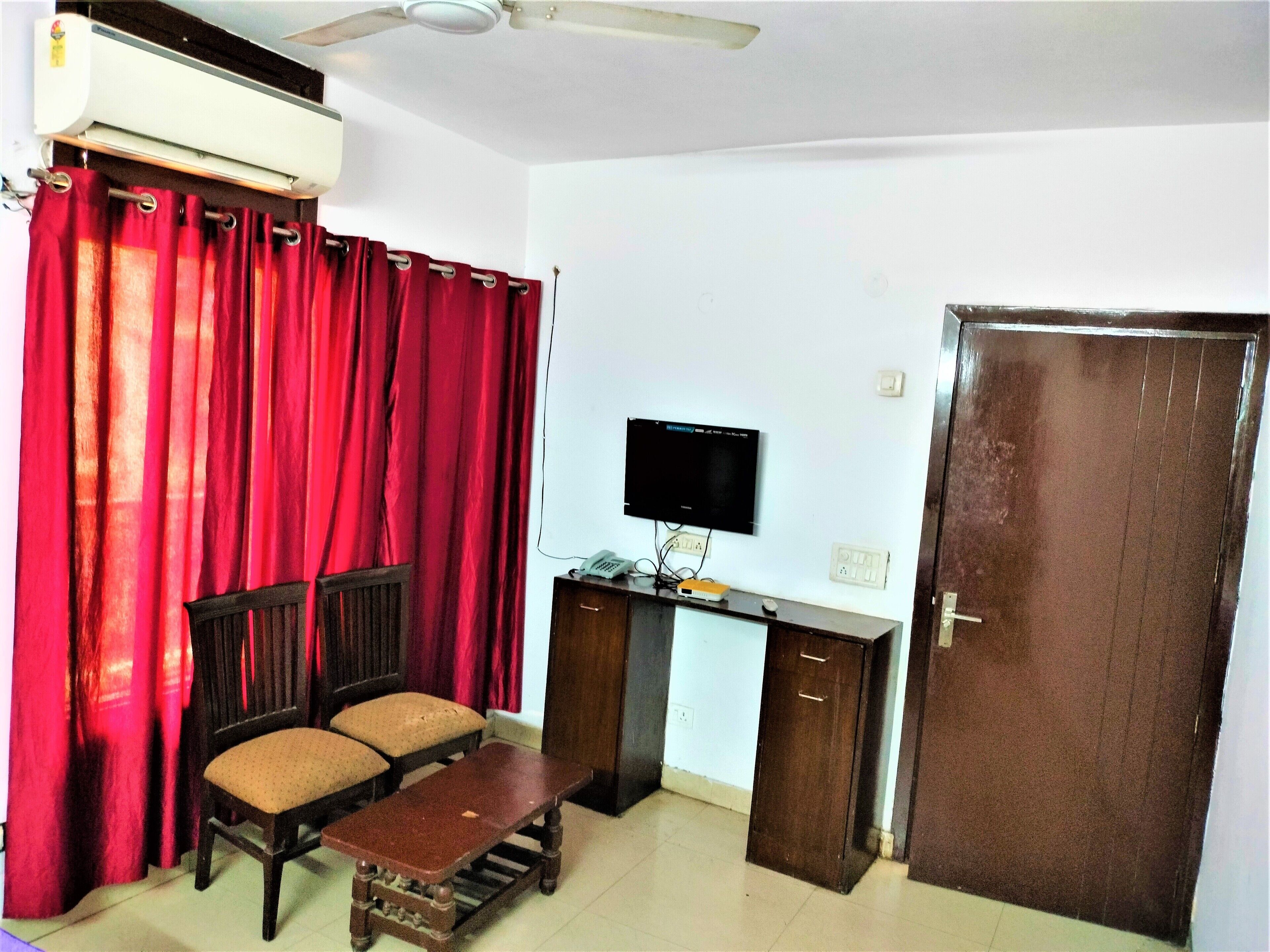A room with a wooden desk, a chair, a television mounted on the wall, and a door.