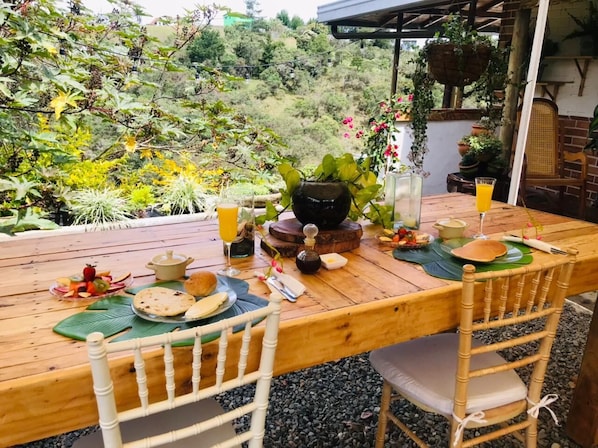 A wooden dining table set outdoors with a view of a garden.