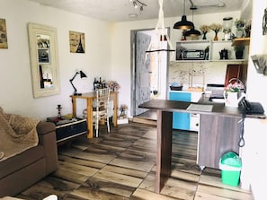 A cozy living room with a wooden floor, a sofa, a dining table with chairs, and a kitchen area with a sink and countertop.