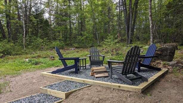 Zona boscosa con terraza de madera y sillas Adirondack.