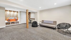 Una sala de estar moderna con un sofá, un sillón de peluche, una silla negra, un revestimiento de pared de madera con estanterías y un pequeño coche de juguete naranja.