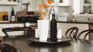 A dining table with a white vase, a black bottle, and a tray.