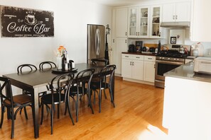 A modern kitchen with white cabinets, a stainless steel refrigerator, and a wooden dining table with chairs.