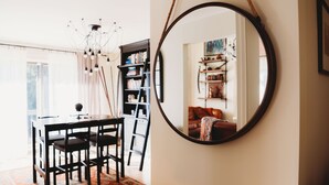 A dining area with a round mirror, a chandelier, and a bookshelf.